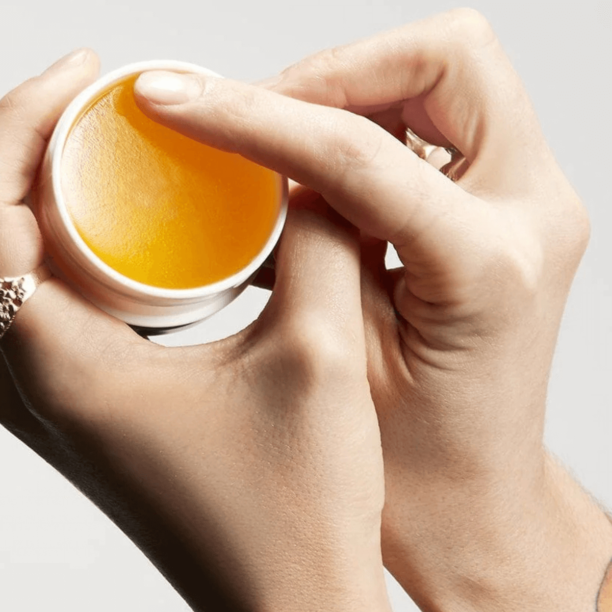 Person tager produkt fra en lille hvid krukke med naturlig gul pomade til håret. Se vores anbefalinger